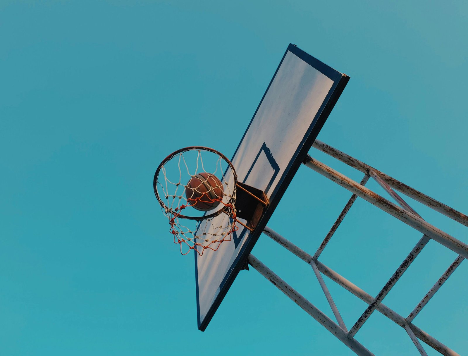 Low angle shot of basketball swishing through a hoop against a clear blue sky.
