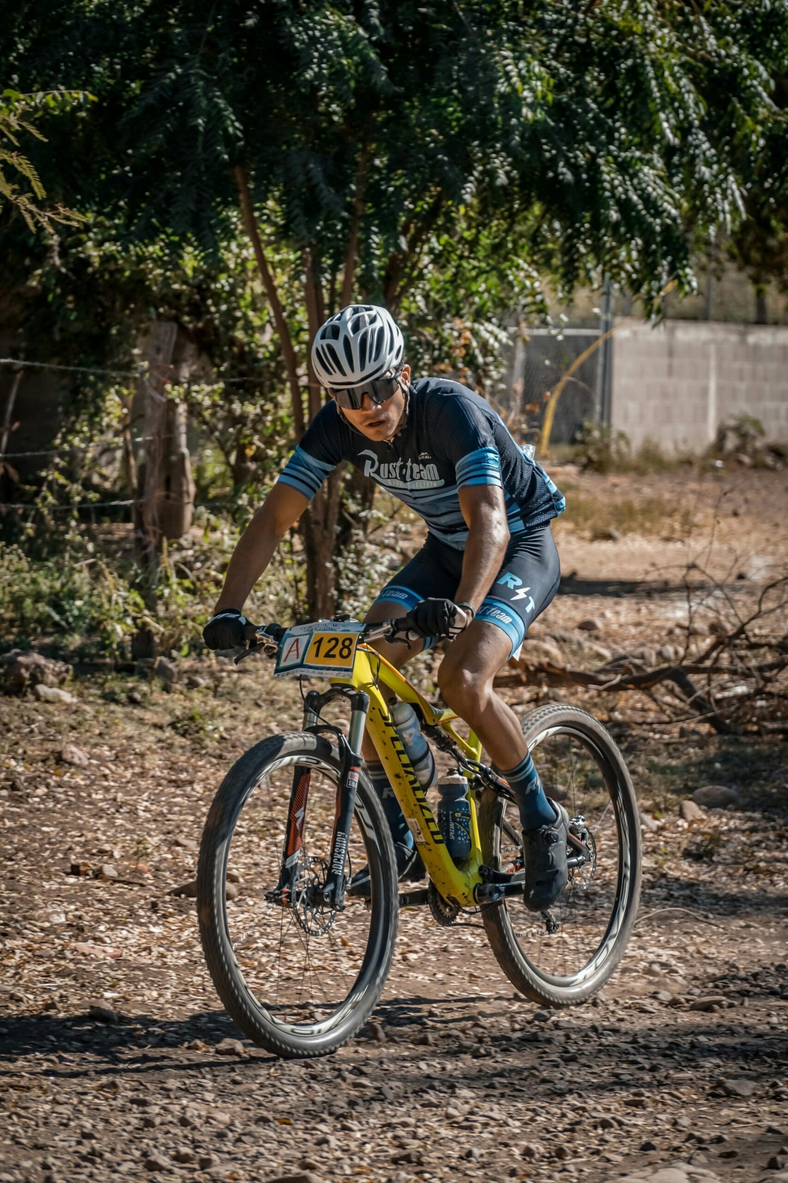 Cyclist riding through rugged terrain in a mountain biking competition under a sunny sky.